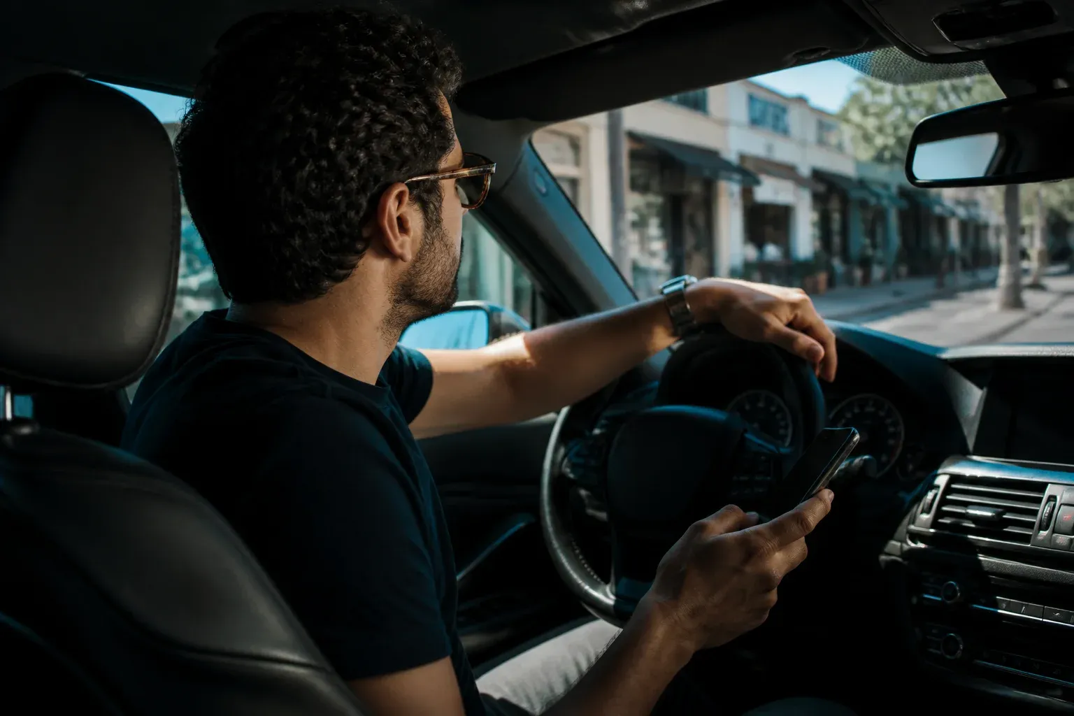 נהג יושב ברכב חונה ומחפש בטלפון עסק קרוב, וברקע חנויות ברחוב